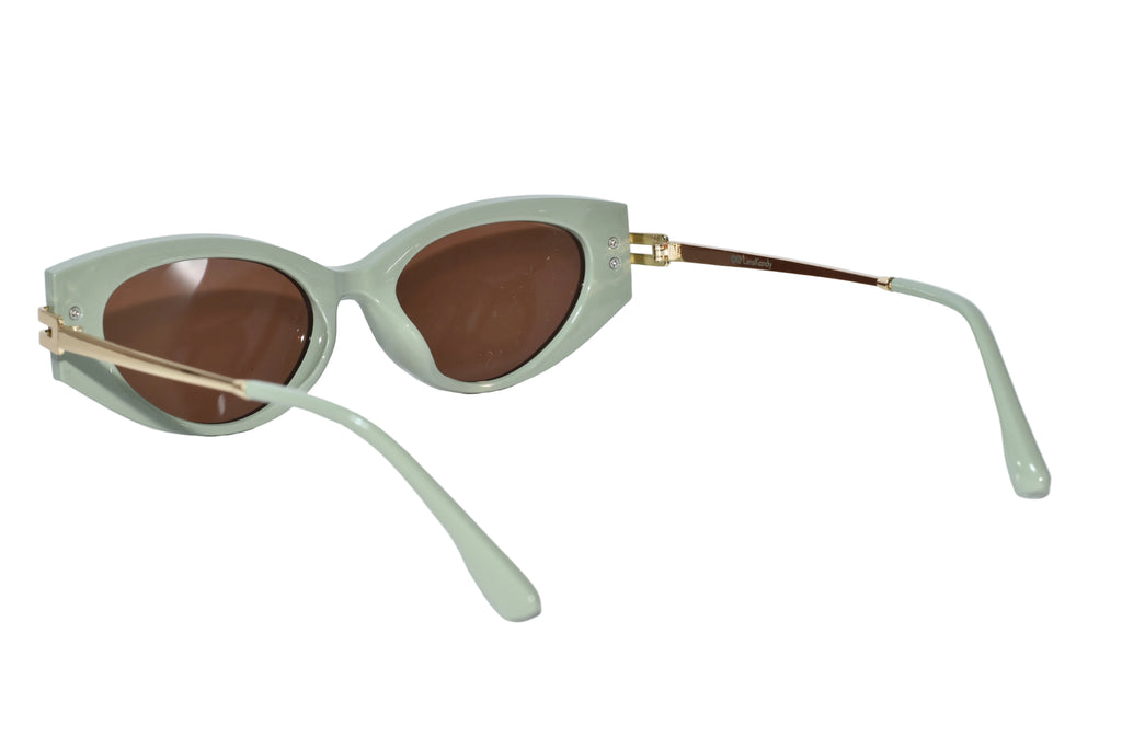 Cat-eye sunglasses with a pale sage green frame, brown tinted lenses, and gold-tone metal temples, displayed on a clean white background.